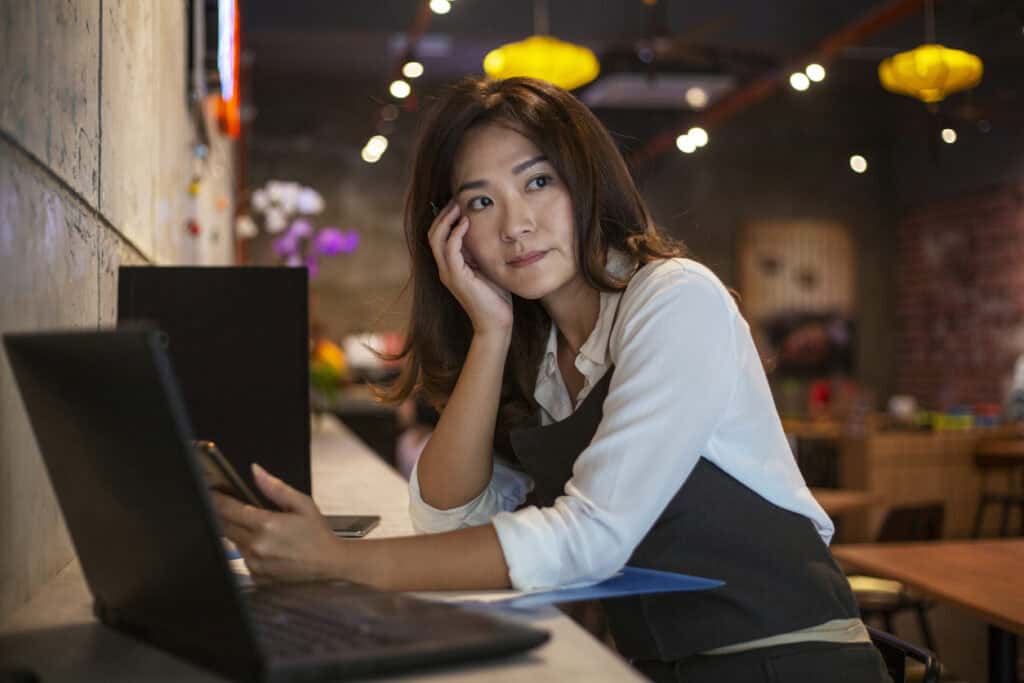 Restaurant owner leans on a counter in front of an open laptop computer looking concerned