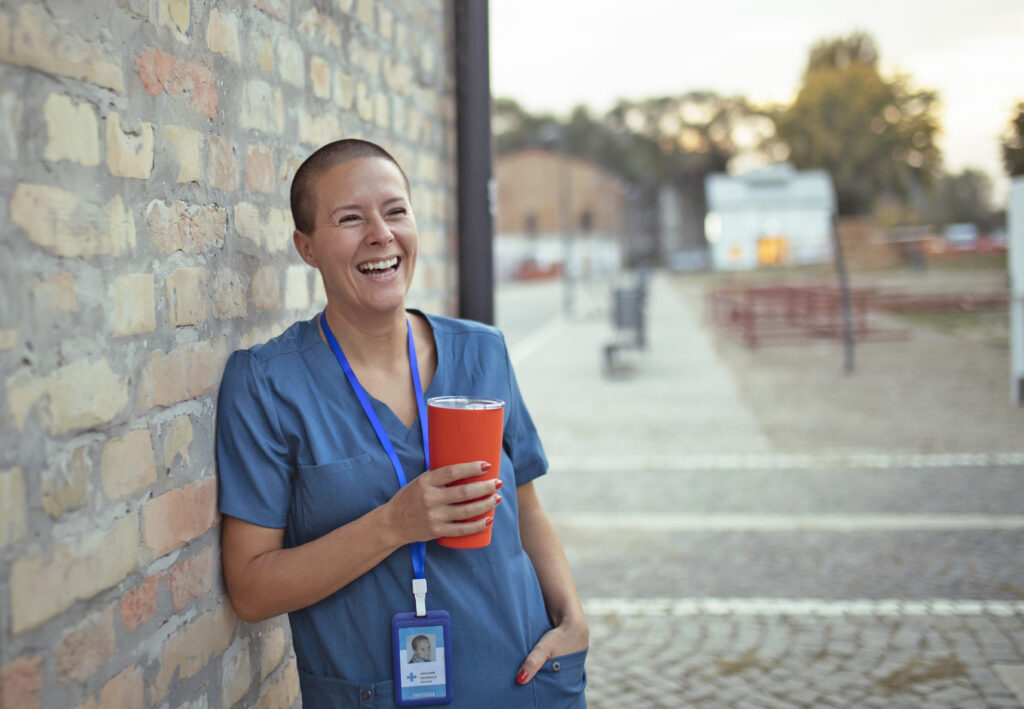 Happy nurse standing outside on their break holding a travel coffee mug