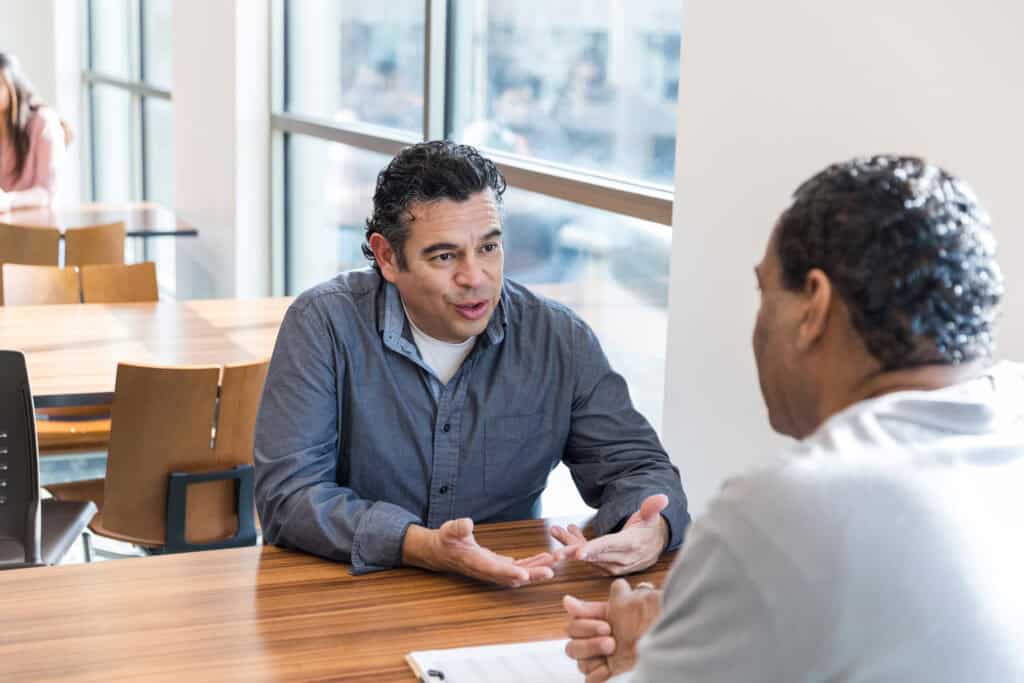 Man talking and gesturing and taking the time to describe how he's feeling to another man he works with
