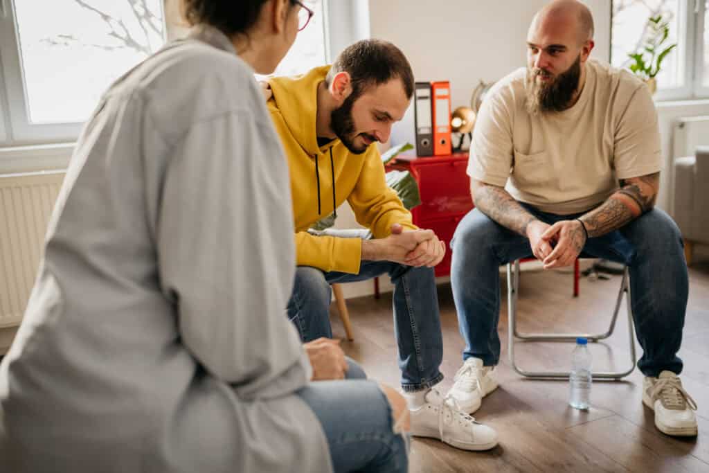 Two men talking in group therapy. A therapist is listening.