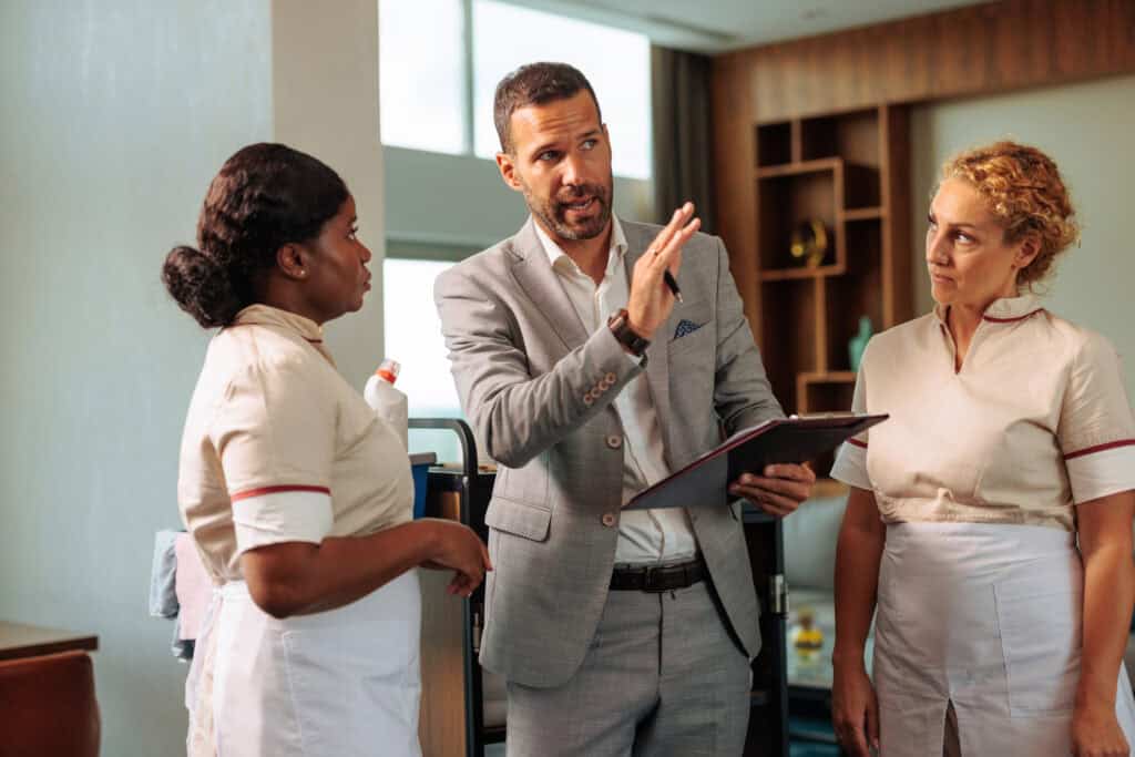 Hotel manager talking to two staff members about an emergency preparedness plan. He is gesturing with his hand to indicate the location of emergency exits.
