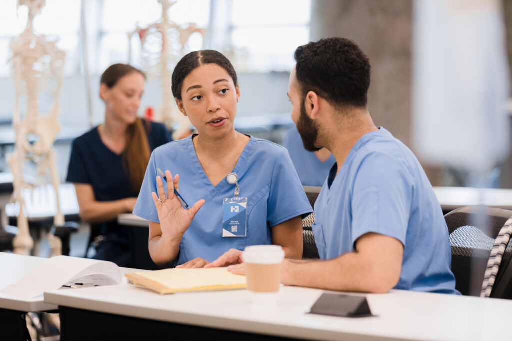 Two nurses talking. one nurse is holding her hand up as she talks and is calmly setting boundaries with the other nurse.