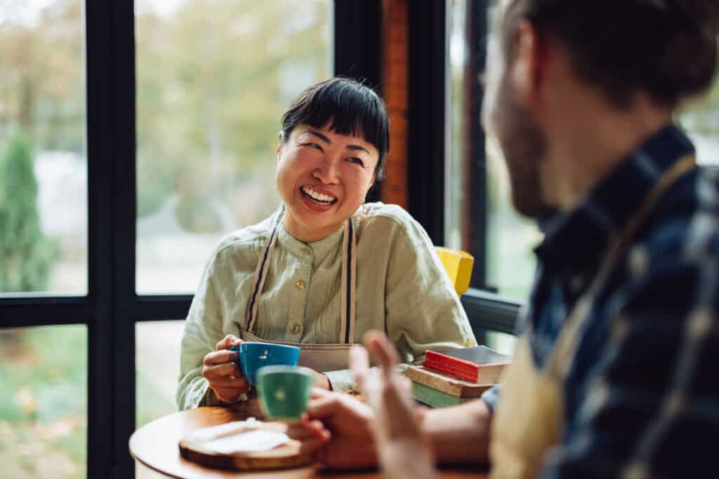 Two cafe workers smiling and chatting at over a cup coffee