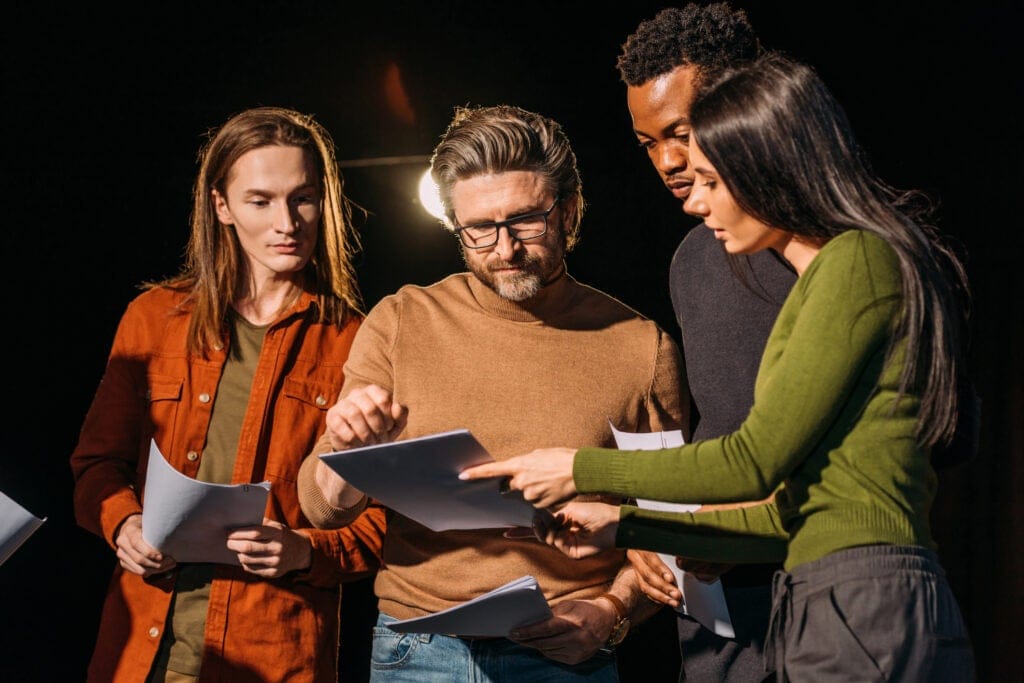 Stage director pointing at a script and having a serious conversation with a group of actors.