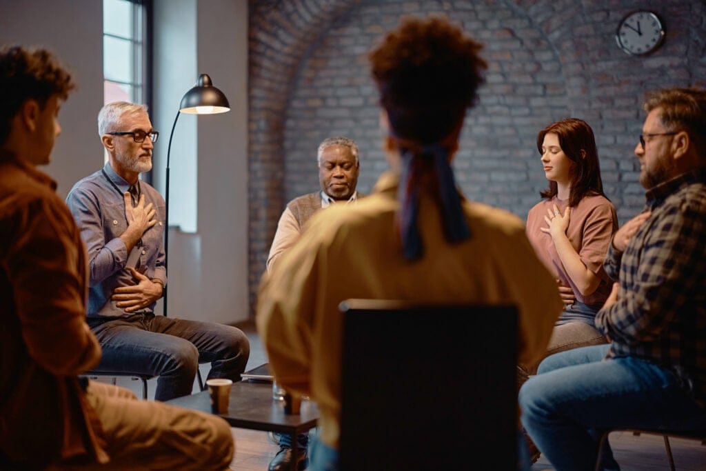 A group of counsellors sitting in a circle with their eyes closed, practicing mindfulness techniques.