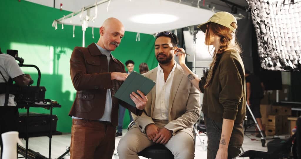 Director talking to an actor with notes about changes to an upcoming scene while the actor is getting their makeup touched up.