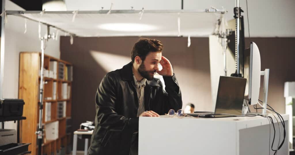 Stressed television director looking at a laptop and running his head.