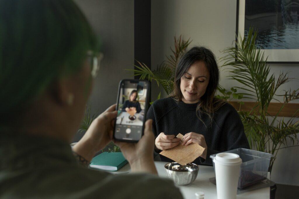 Indigenous woman crafting with birch bark while her friend live streams on her phone