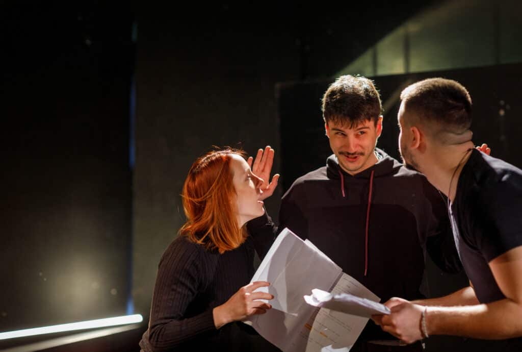 Actors standing on a stage, having a discussion about a script.