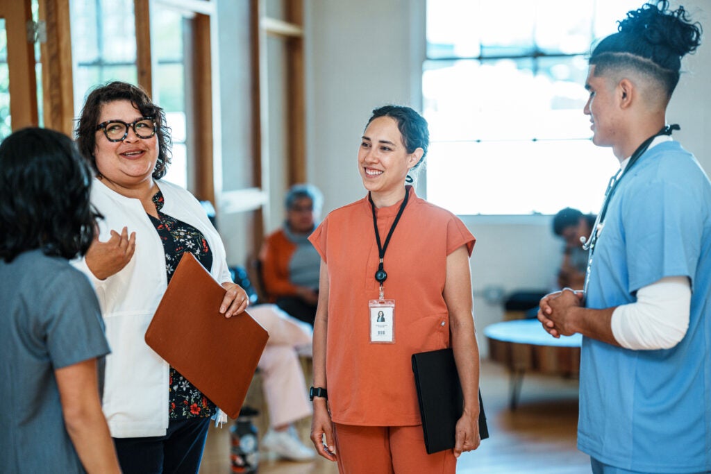 A diverse group of doctors stand in a sunny corridor talking and smiling.