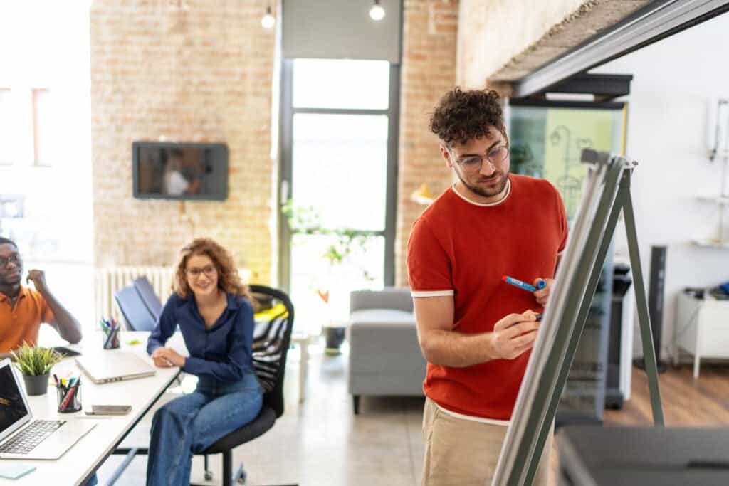 Social worker writes plans on a whiteboard while his colleagues sitting at a conference table look on.