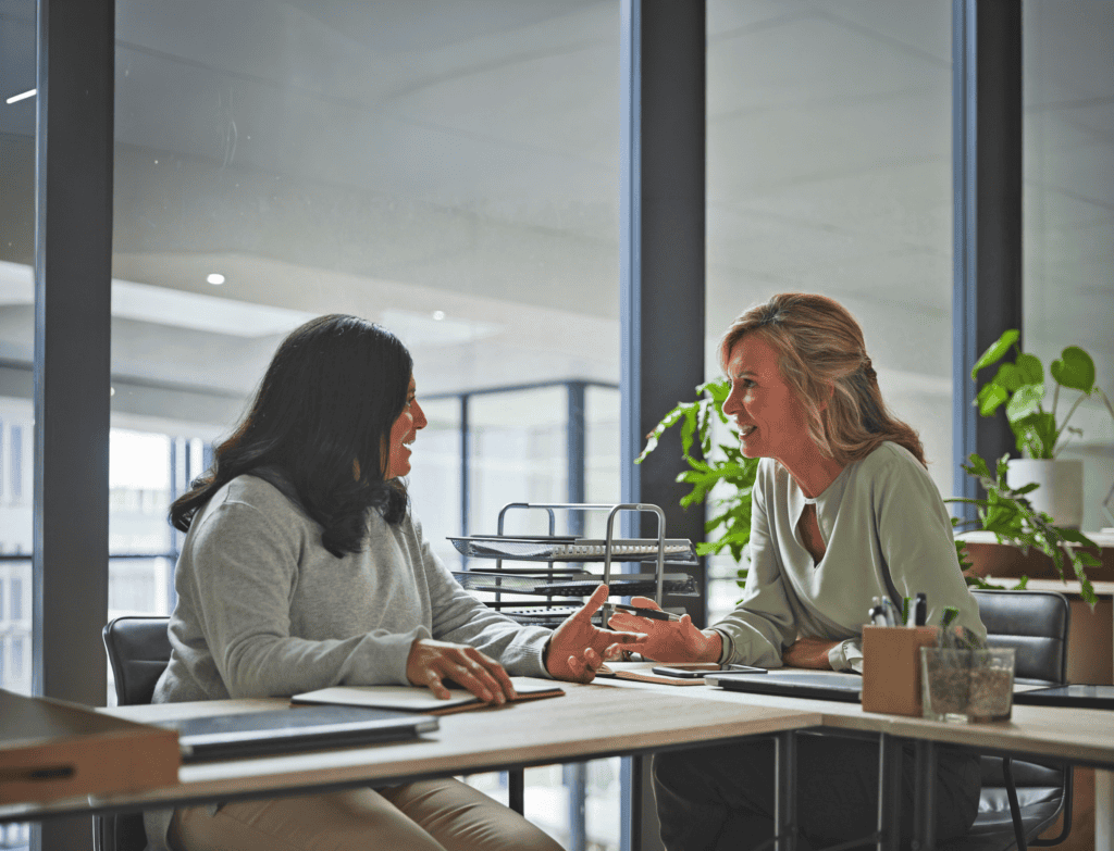 A manager and employee sitting at a table in an office. The manager is providing the employee with supportive information.