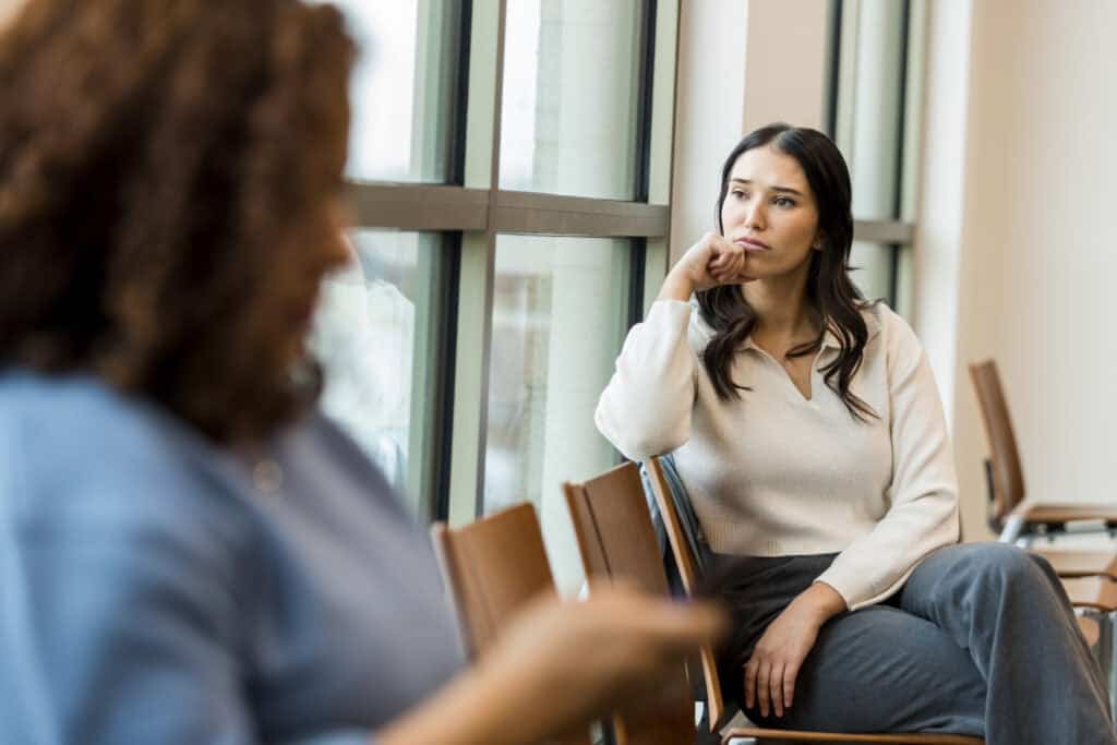 Young woman social worker sitting by a window looking worried and distracted.