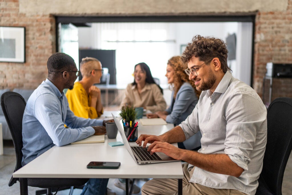 Neurodivergent man working on a laptop with a group of his peers in a casual office setting.