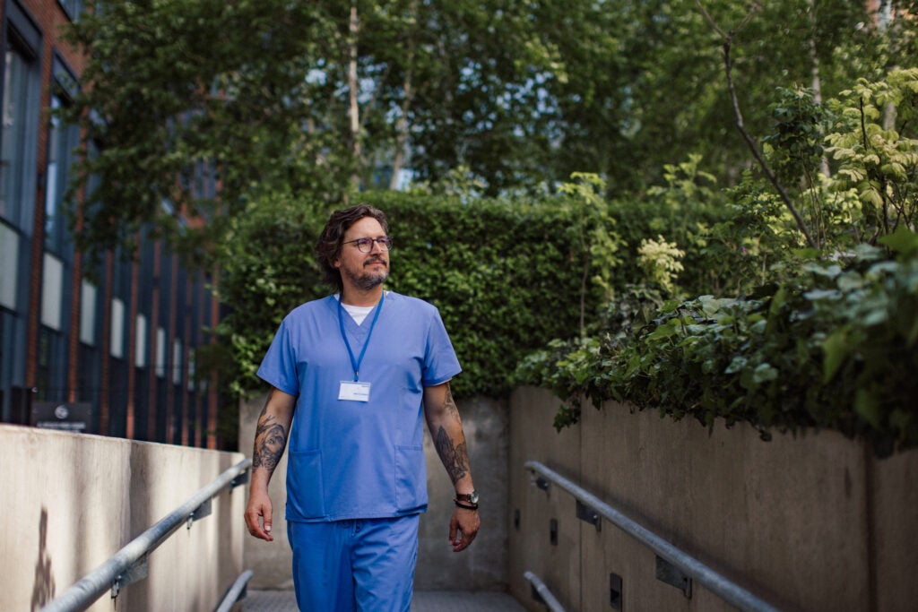 Male nurse going home from work, walking in front of hospital building.