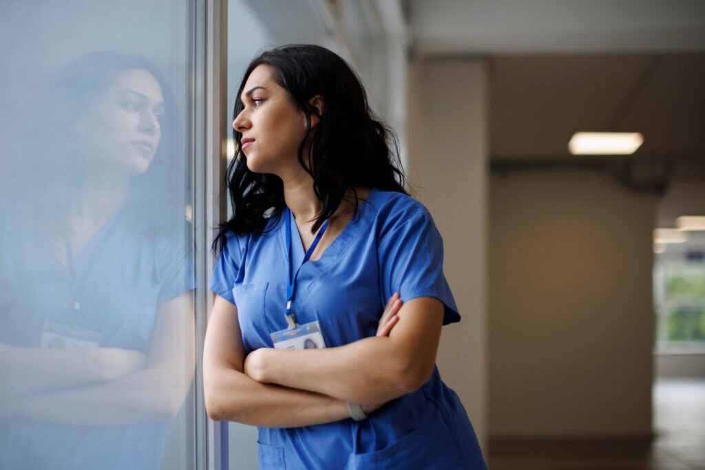 Nurse taking a moment during a hectic day to pause and think while looking out the window in a quiet hallway.